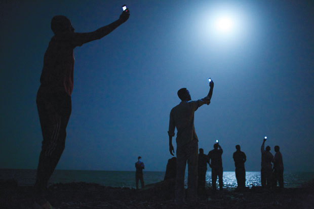 A foto do ano: Imagem reflete sobre impacto atual de telefones celulares. A foto do americano John Staneyer levou o Grande Prêmio de 2014 ao retratar migrantes africanos na praia da capital do Djibouti, com celulares nas mãos, em busca de sinal barato da vizinha Somália. “Ela abre discussões sobre tecnologia, globalização, migração, pobreza, desespero, alienação e humanidade”, afirmou a jurada Jillian Edelstein | John Stanmeyer/VII/National Geographic