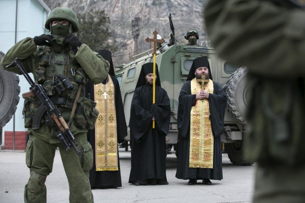 Monges ortodoxos rezam próximos de militares armados e blindados russos na região da Crimeia | Baz Ratner/Reuters