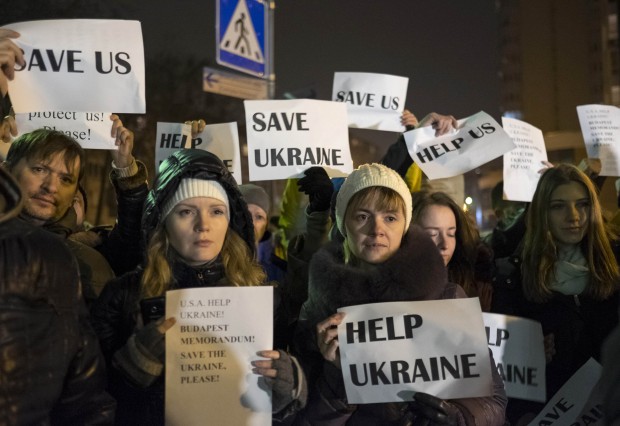 Ucranianos reunidos diante da embaixada das EUA em Kiev seguram cartazes onde se lê: ajudem a Ucrânia e Salvem a Ucrânia | Gleb Garanich/Reuters