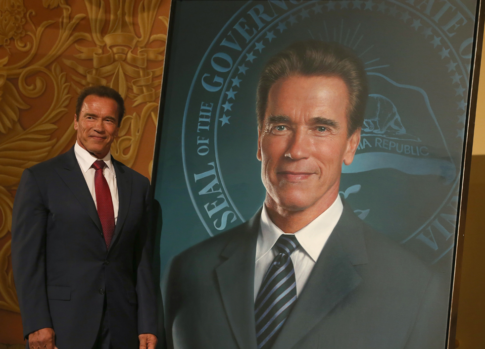 Ex-governador da Califórnia Arnold Schwarzenegger ao lado da pintura oficial | Justin Sullivan/Getty Images